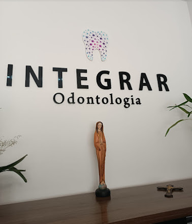 Recepção da Integrar Odontologia, com o logo na parede, plantas e um balcão de madeira